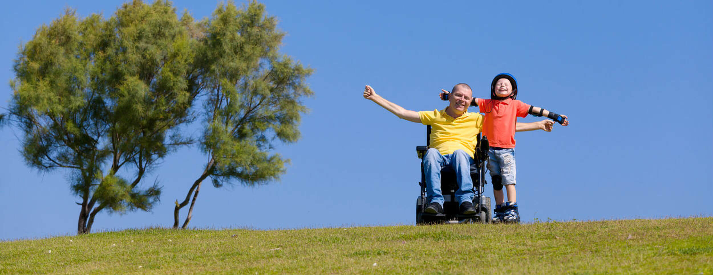 Happy man in a wheelchair with a young boy on a hill in the sun