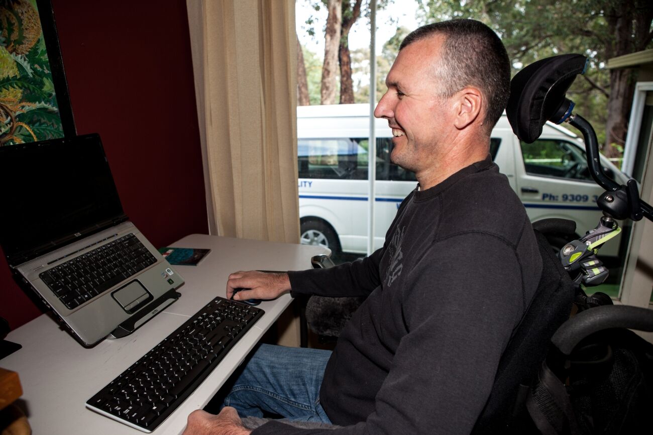 Smiling man looking at a computer sitting comfortably in a wheel chair